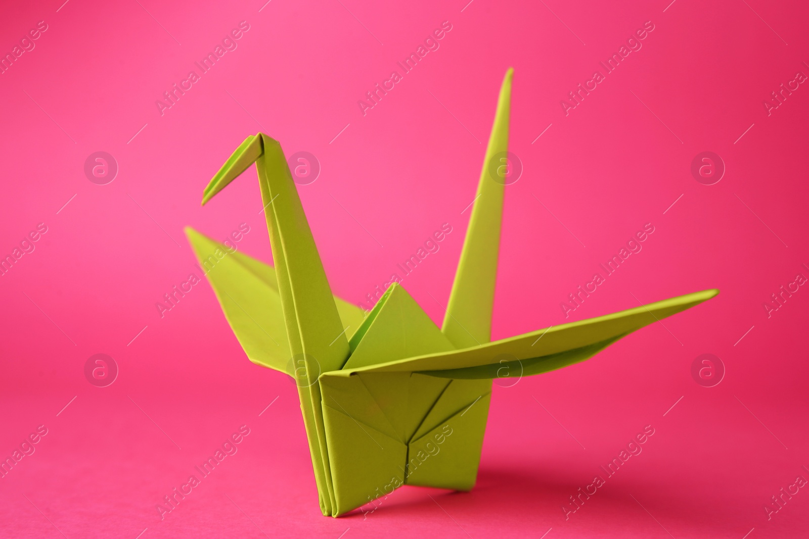 Photo of Origami art. Handmade paper crane on pink background, closeup