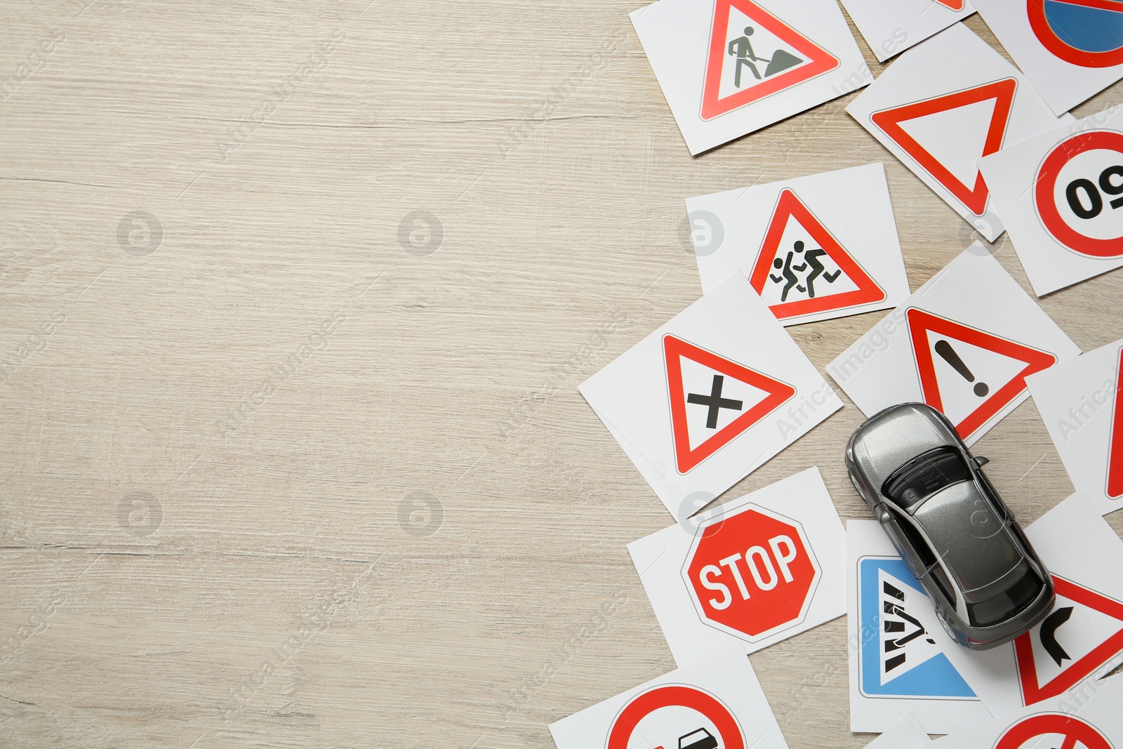 Photo of Many different road sign cards and toy car on wooden table, flat lay with space for text. Driving school