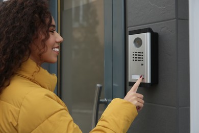 Photo of Young African-American woman ringing intercom with camera near building entrance