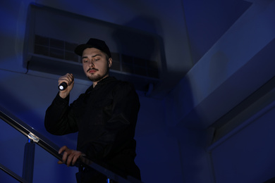 Photo of Male security guard with flashlight on stairs in darkness