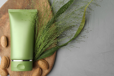 Photo of Tube of cosmetic product, plant and almond nuts on grey table, flat lay