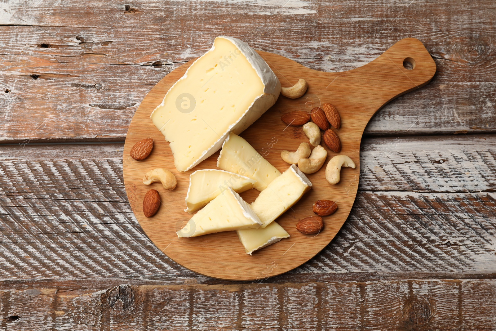 Photo of Tasty Camembert cheese with nuts on wooden table, top view