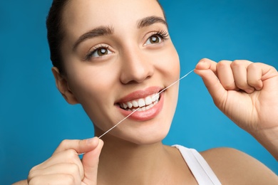 Photo of Young woman flossing her teeth on blue background. Cosmetic dentistry