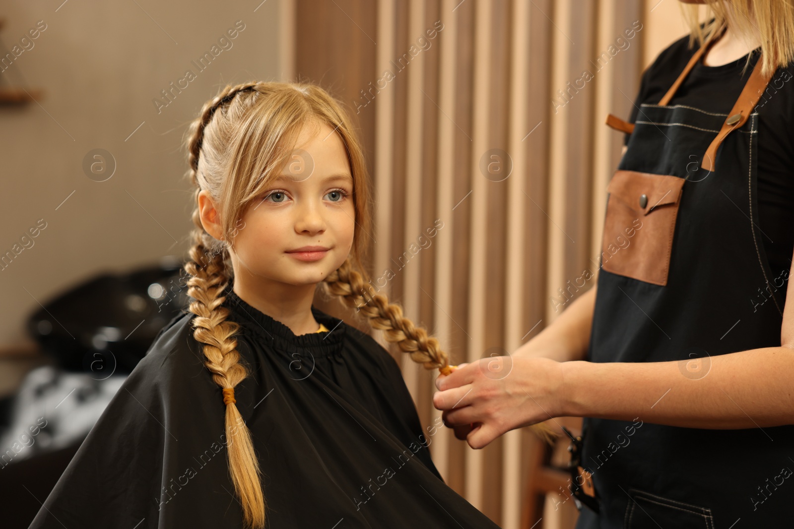 Photo of Professional hairdresser braiding girl's hair in beauty salon