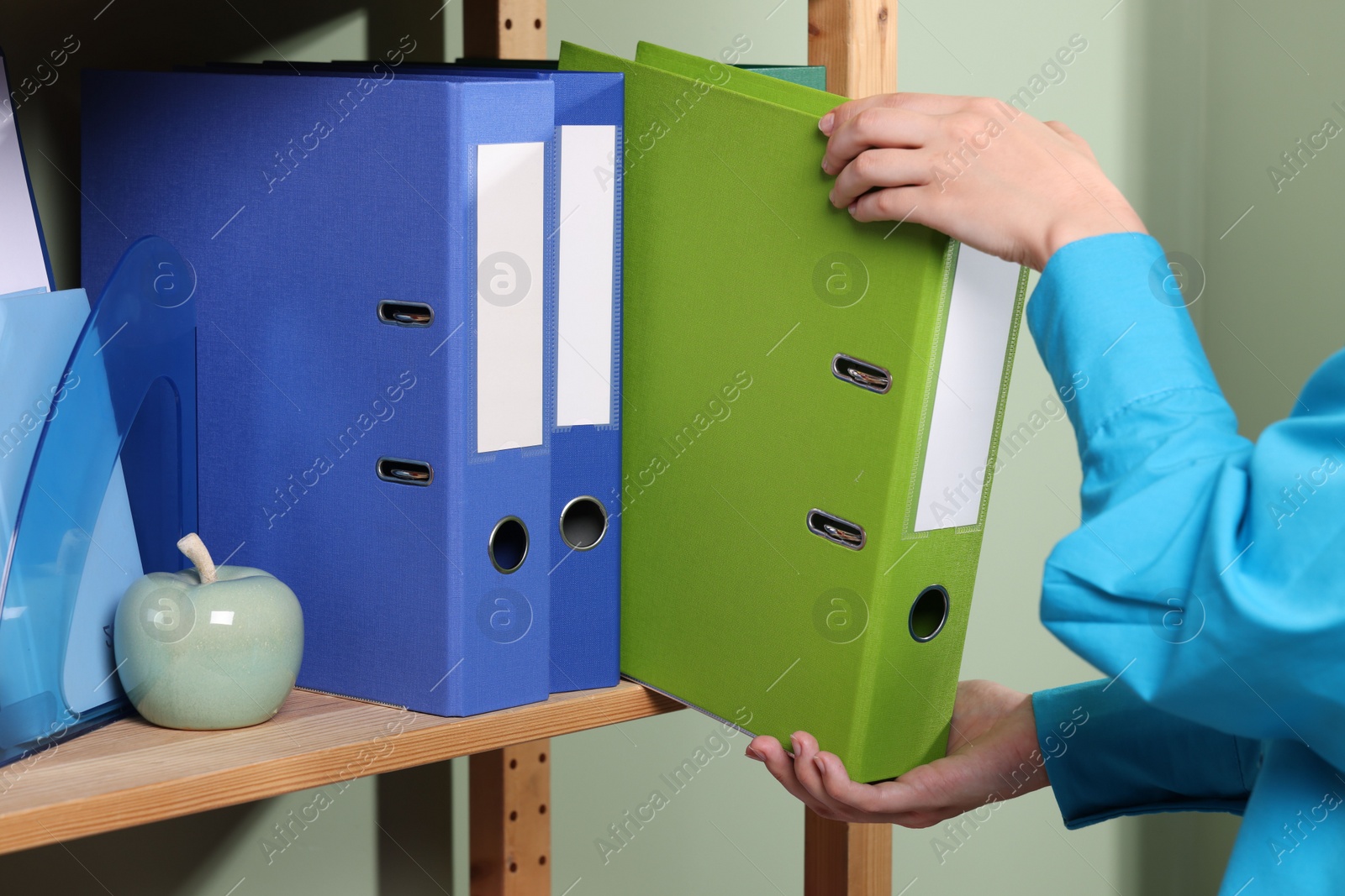 Photo of Woman taking binder office folder from shelving unit indoors, closeup