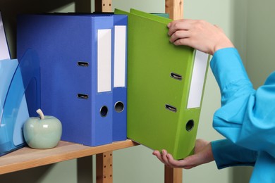 Woman taking binder office folder from shelving unit indoors, closeup