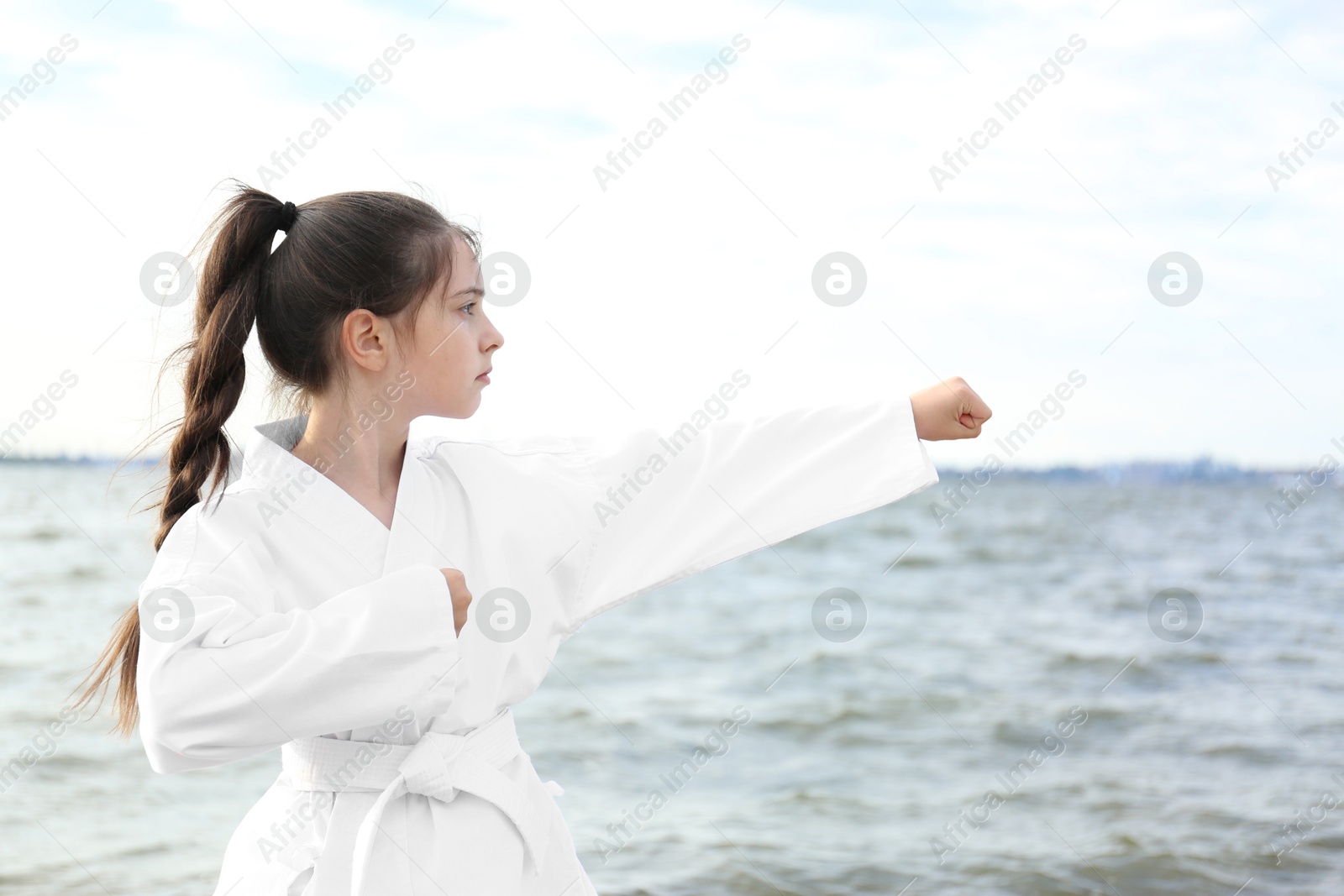 Photo of Cute little girl in kimono practicing karate near river