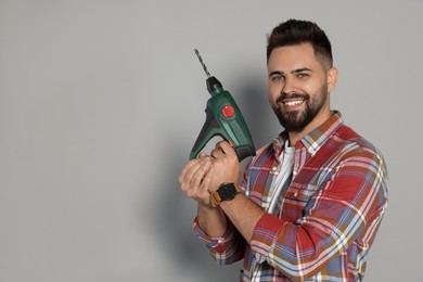 Photo of Young man with power drill on grey background. Space for text
