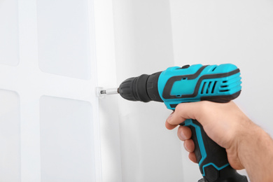 Photo of Worker installing kitchen furniture with electric screwdriver, closeup