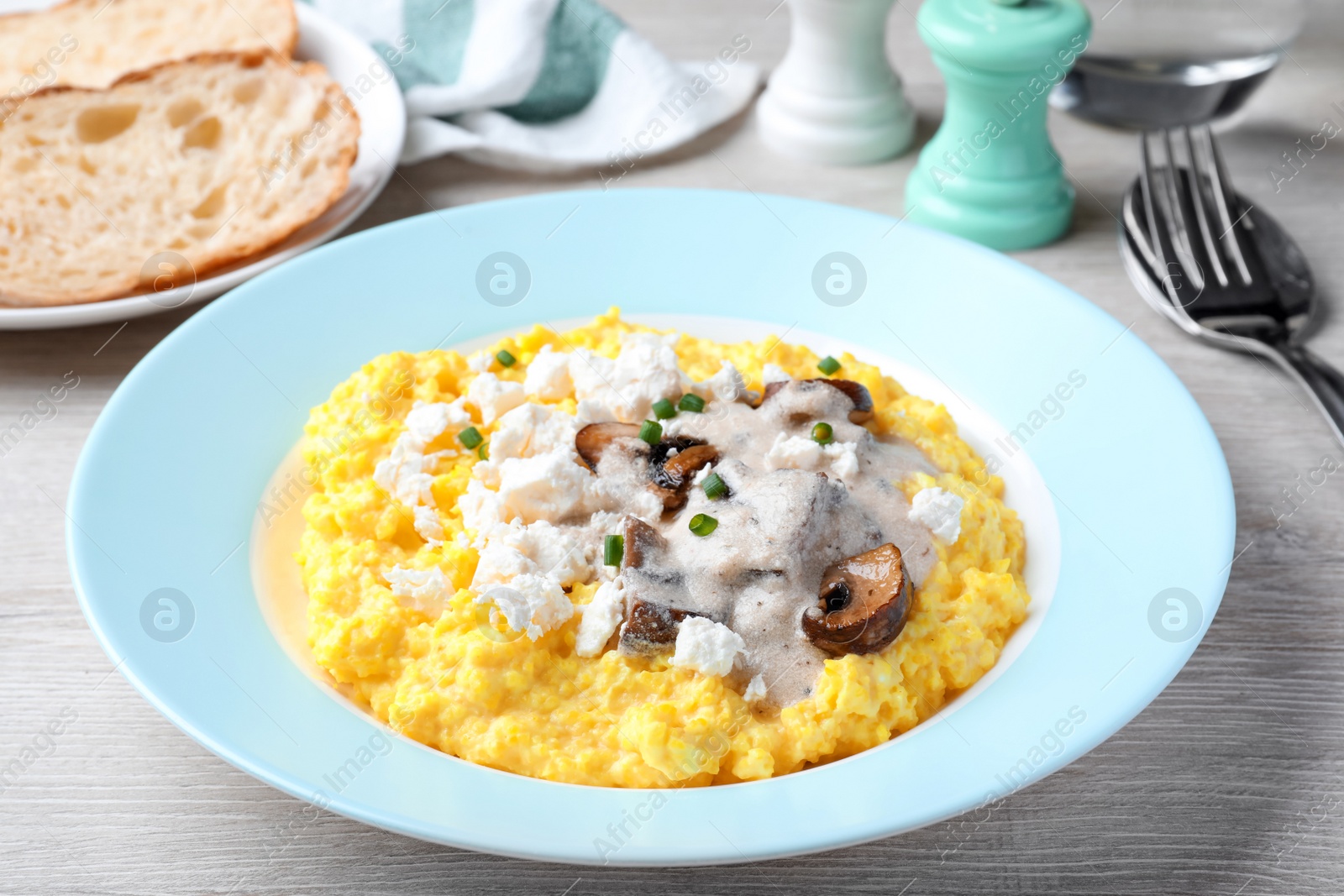 Photo of Tasty banosh served with brynza and mushrooms on light wooden table, closeup. Traditional Ukrainian dish