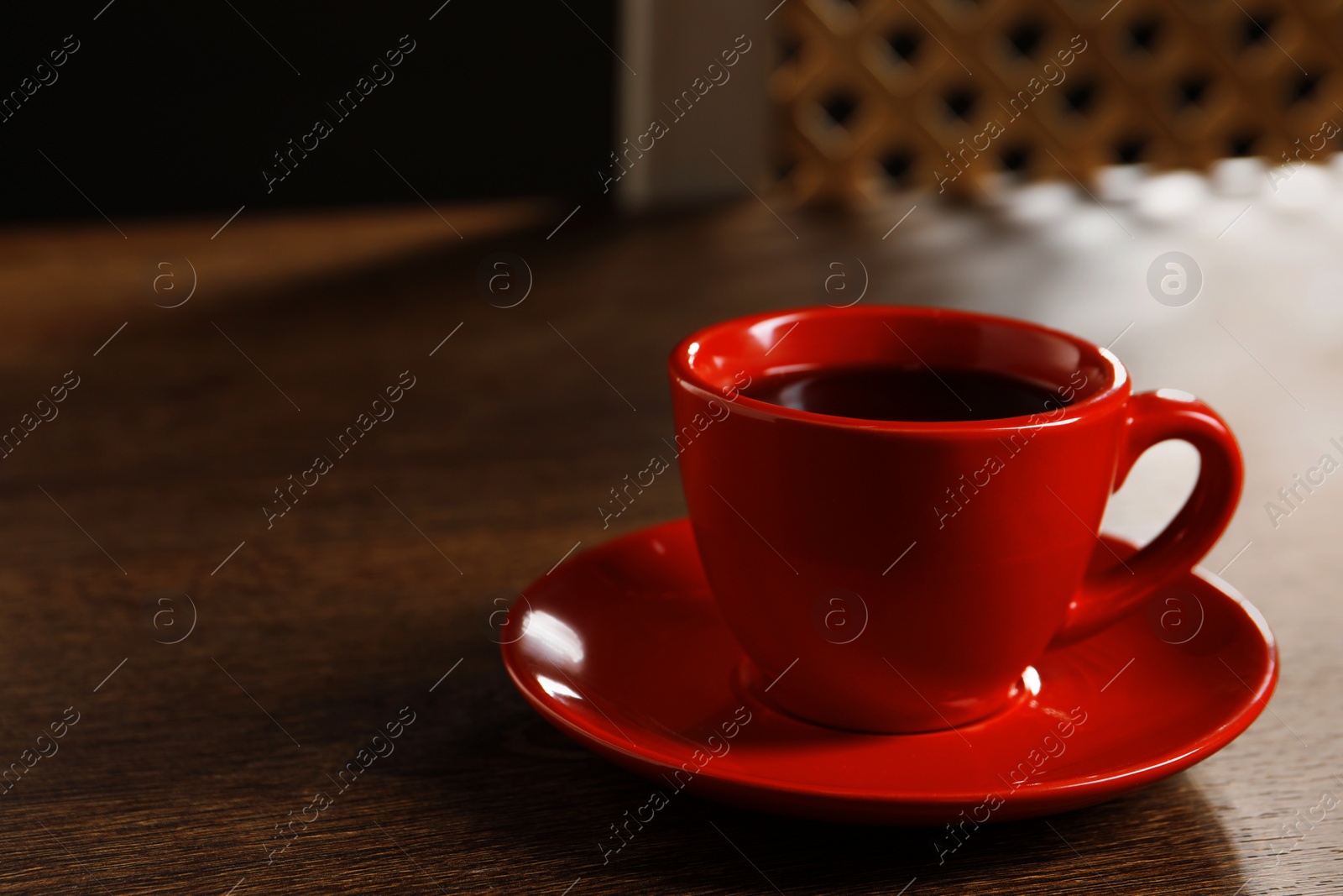 Photo of Red cup with aromatic coffee on wooden table indoors. Space for text