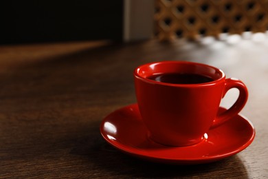 Red cup with aromatic coffee on wooden table indoors. Space for text