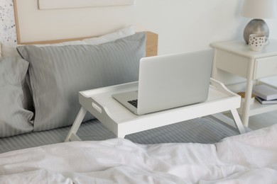 Photo of White tray table with laptop on bed indoors