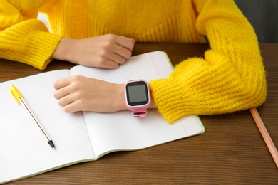 Photo of Girl with stylish smart watch at wooden table in school, closeup