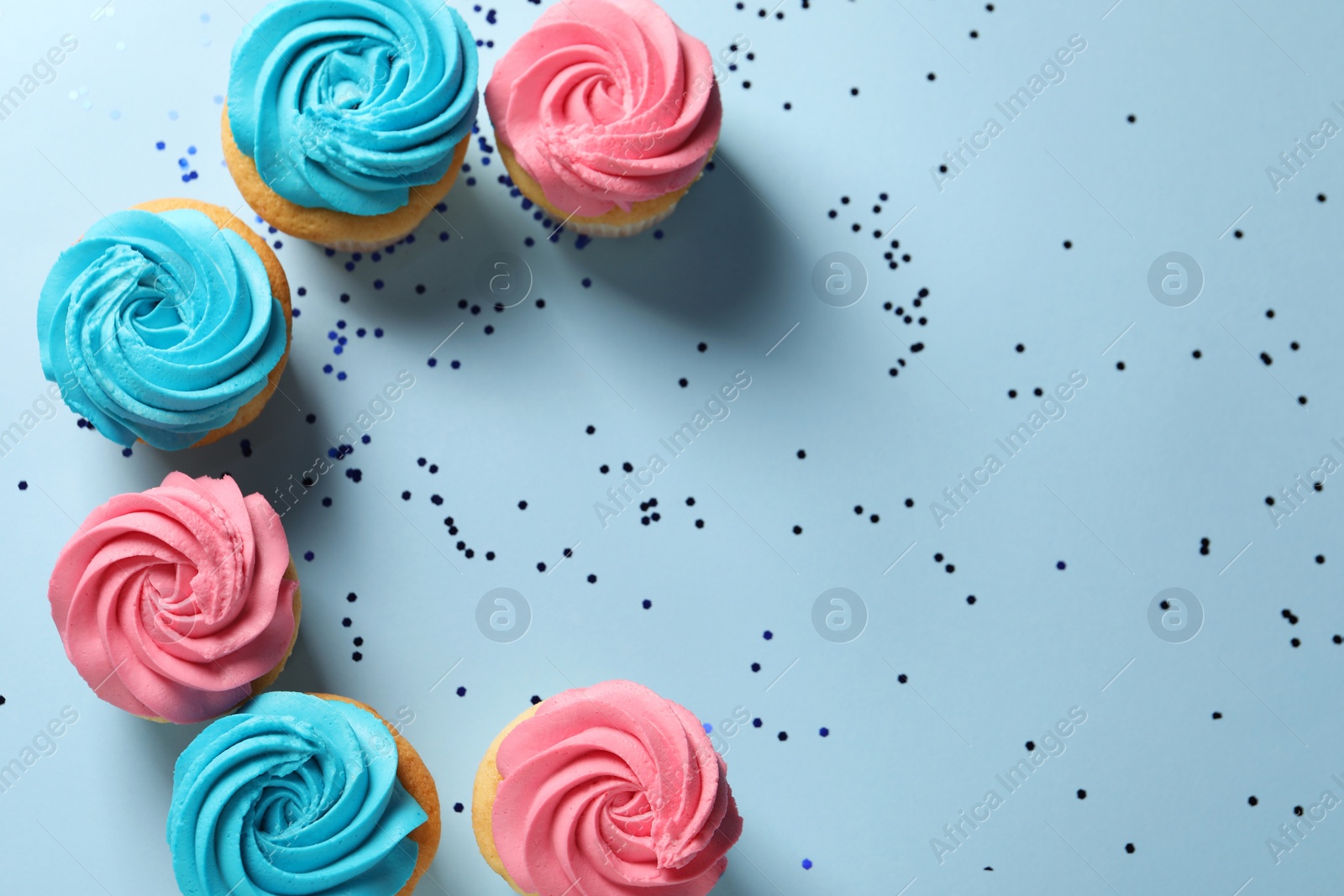 Photo of Delicious cupcakes with bright cream and confetti on light blue background, flat lay. Space for text