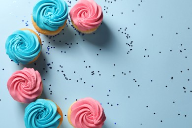 Photo of Delicious cupcakes with bright cream and confetti on light blue background, flat lay. Space for text