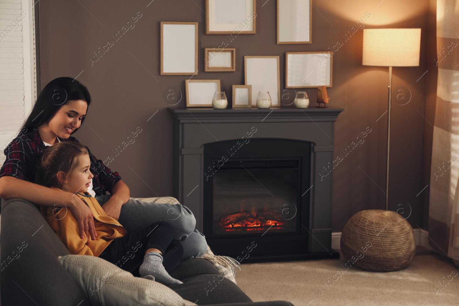 Photo of Happy mother and daughter spending time together on sofa near fireplace at home. Space for text