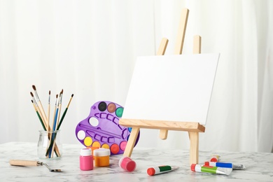 Photo of Wooden easel with blank canvas board and painting tools for children on table in room