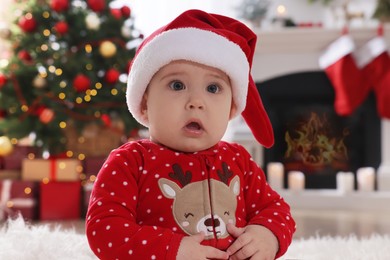 Photo of Baby in Santa hat and bright Christmas pajamas at home