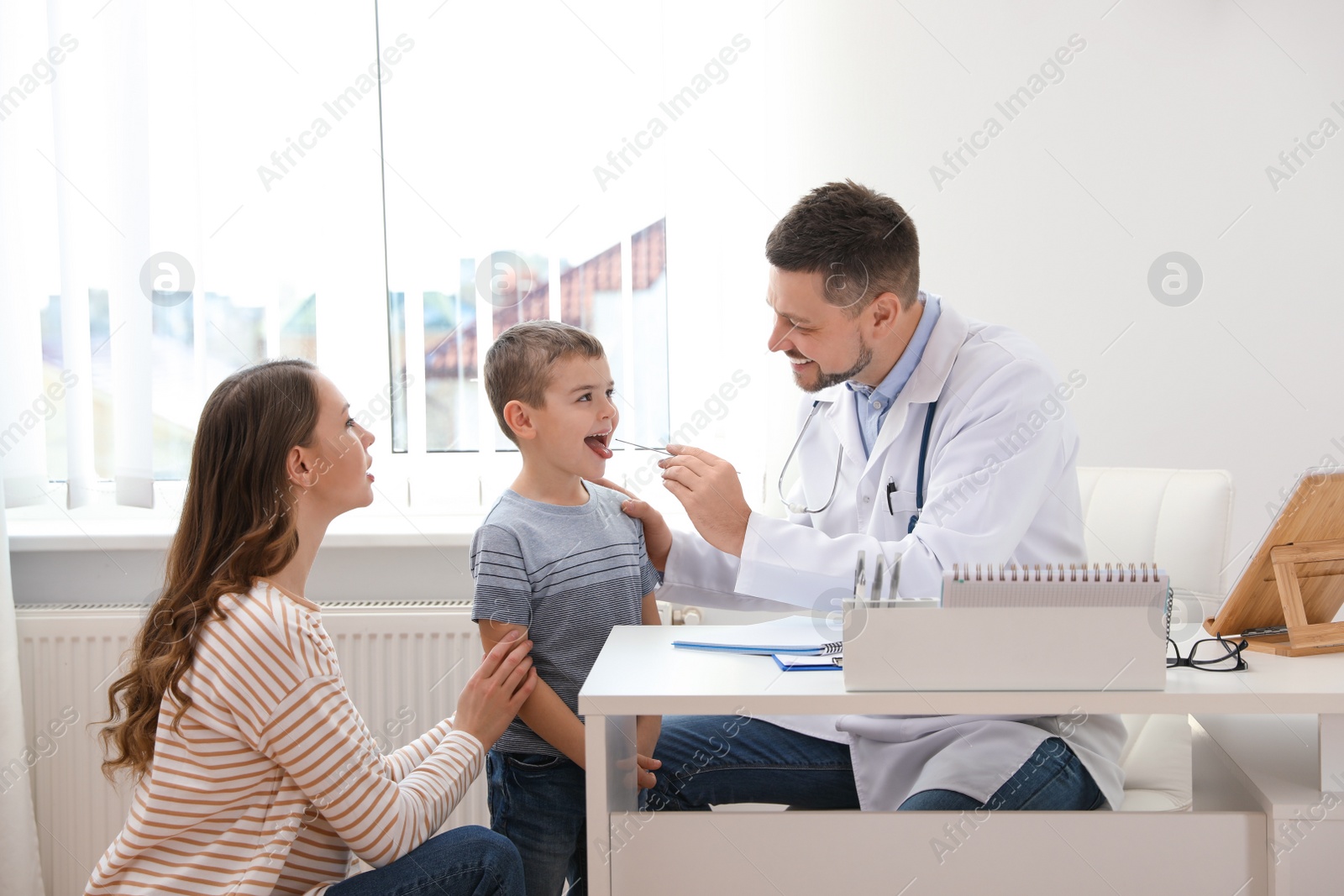 Photo of Mother and son visiting pediatrician. Doctor examining little patient's throat in hospital