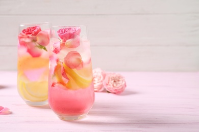 Photo of Delicious refreshing drink with lemon and roses on pink wooden table. Space for text
