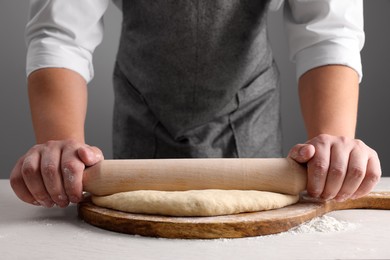 Photo of Man rolling dough with wooden pin at white table near grey wall, closeup