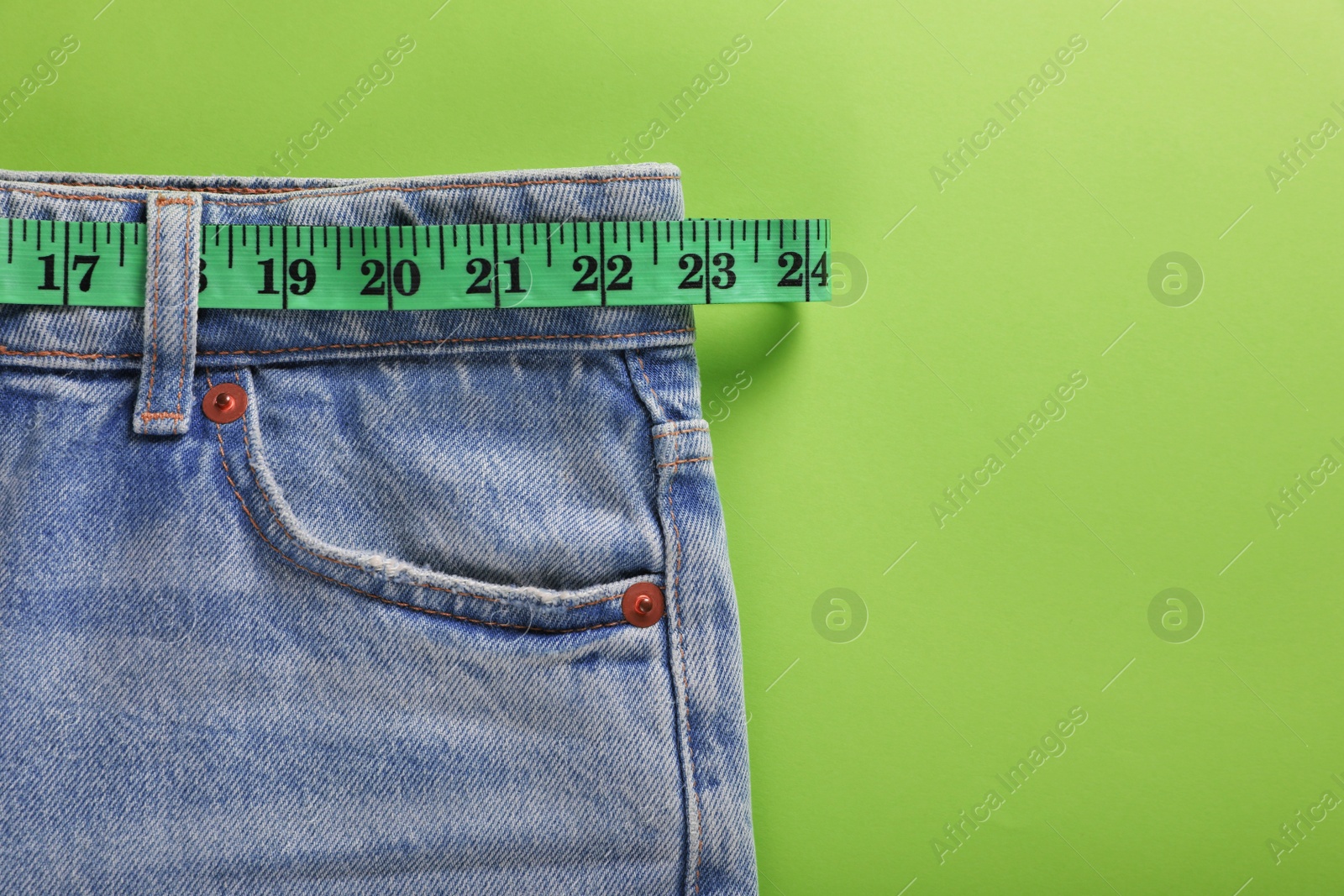 Photo of Jeans and measuring tape on light green background, top view with space for text. Weight loss concept