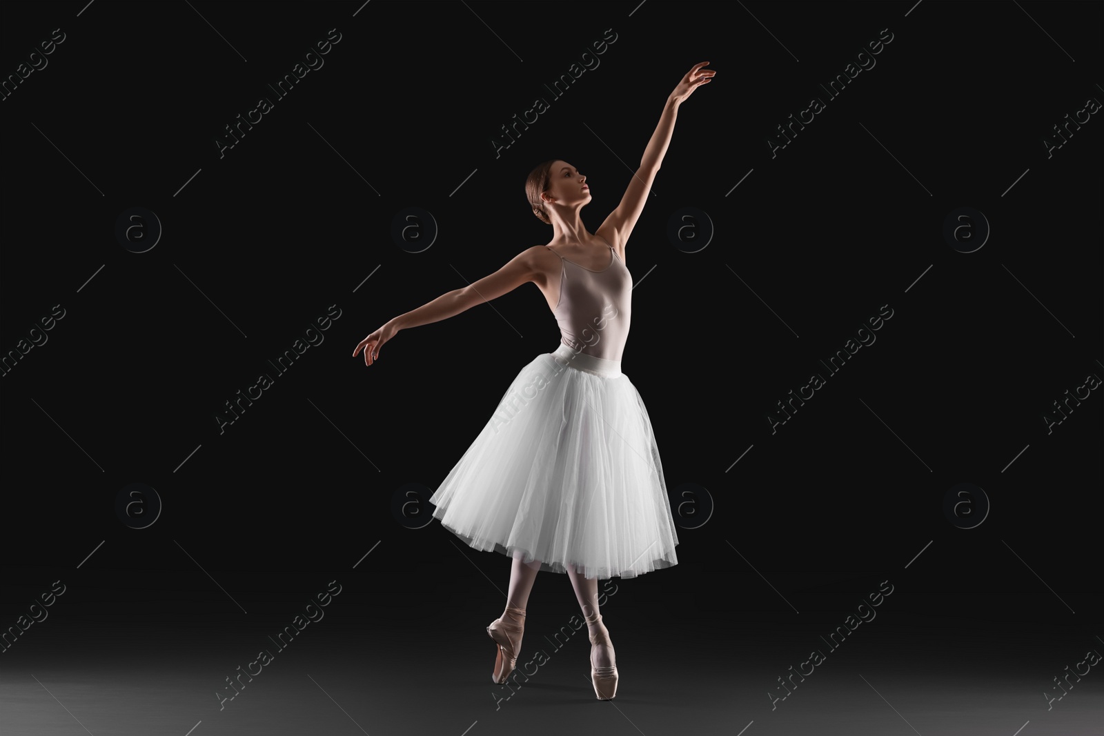 Photo of Young ballerina practicing dance moves on black background