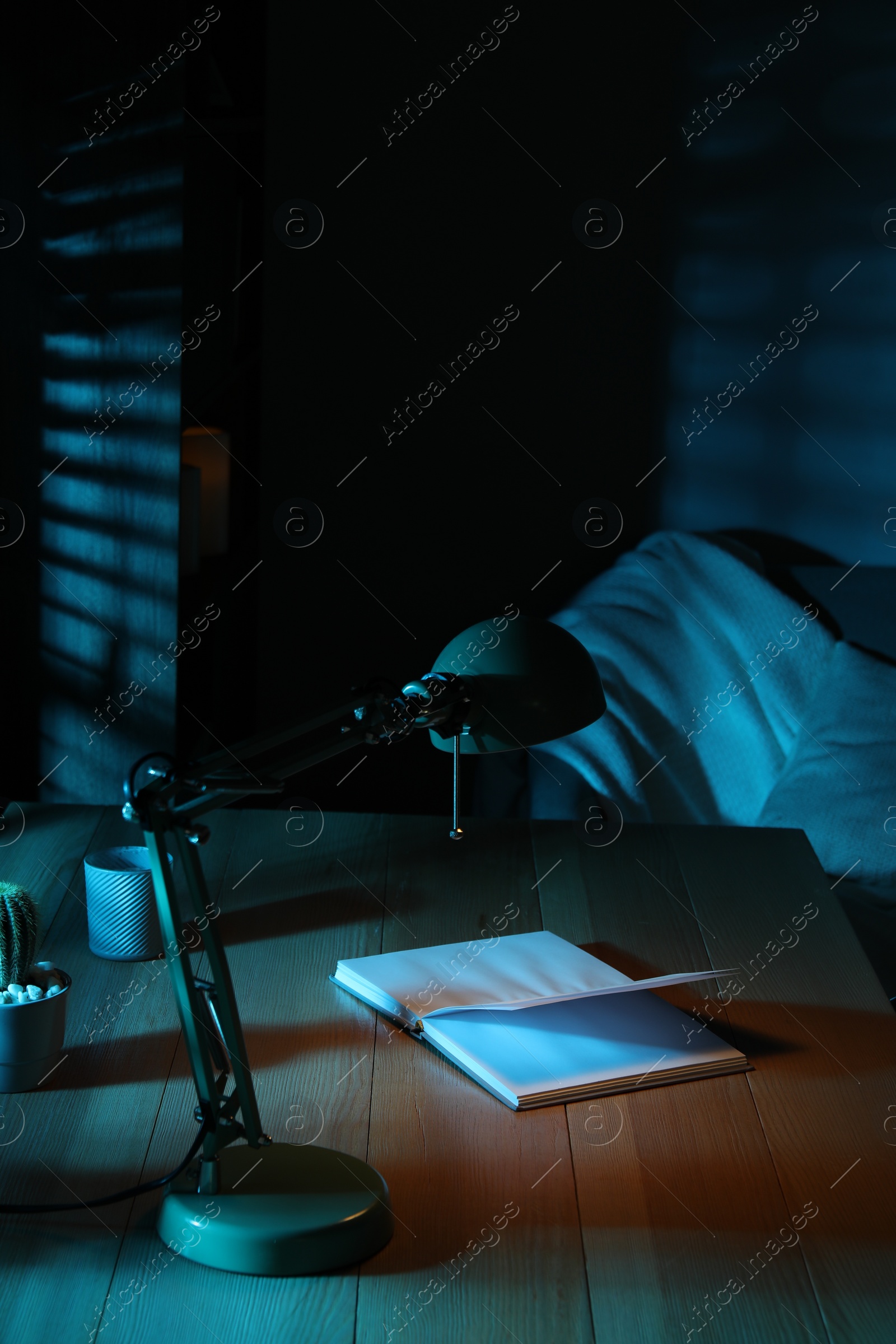 Photo of Stylish lamp and open book on wooden table at night