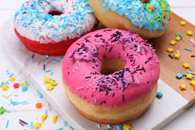 Photo of Sweet glazed donuts decorated with sprinkles on white table, closeup. Tasty confectionery