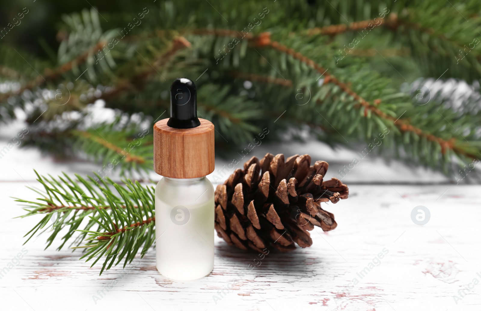 Photo of Bottle of pine essential oil, conifer tree branches and cone on white wooden table