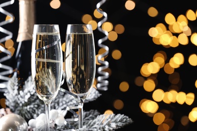 Glasses of champagne and serpentine streamers against black background with blurred lights. Space for text