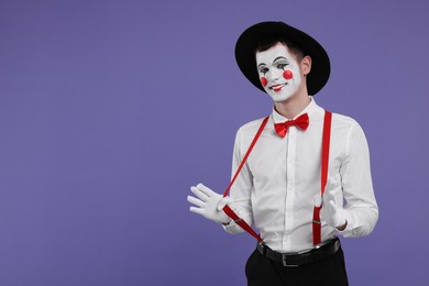 Photo of Funny mime artist in hat posing on purple background. Space for text