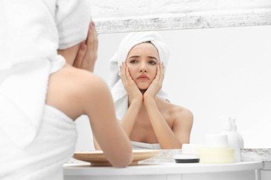 Photo of Teenage girl with acne problem looking in mirror indoors