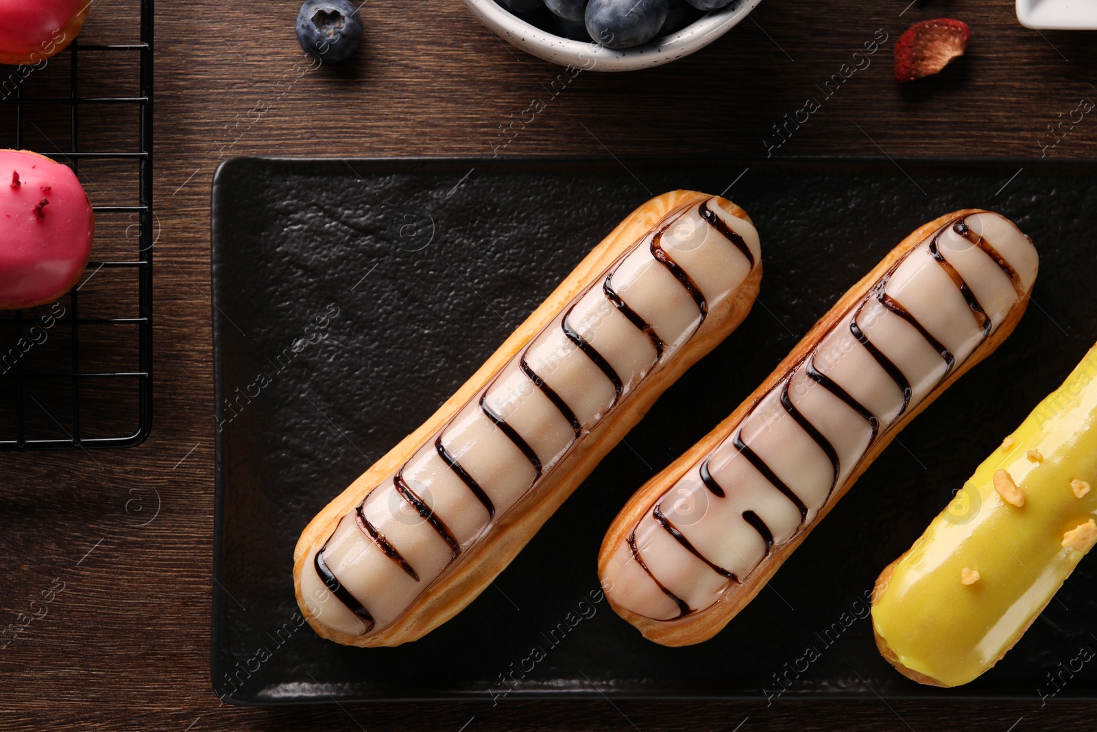 Photo of Different tasty glazed eclairs on wooden table, flat lay