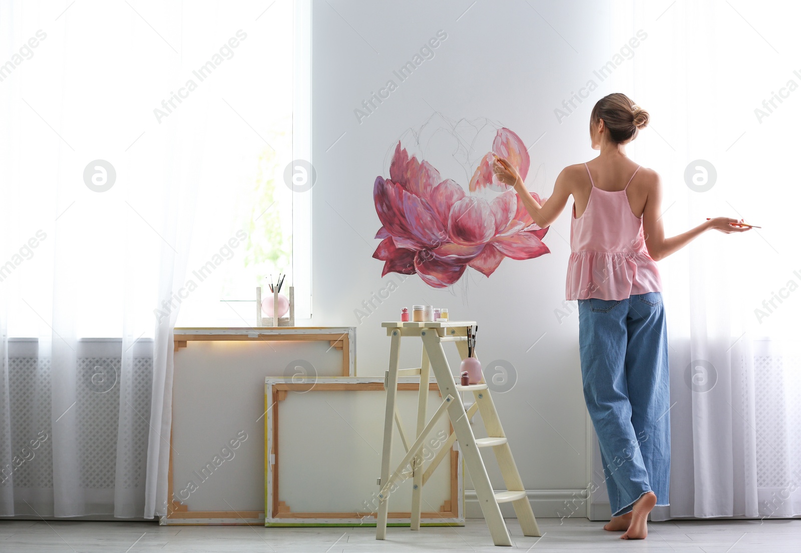 Photo of Decorator painting flower on white wall in room. Interior design