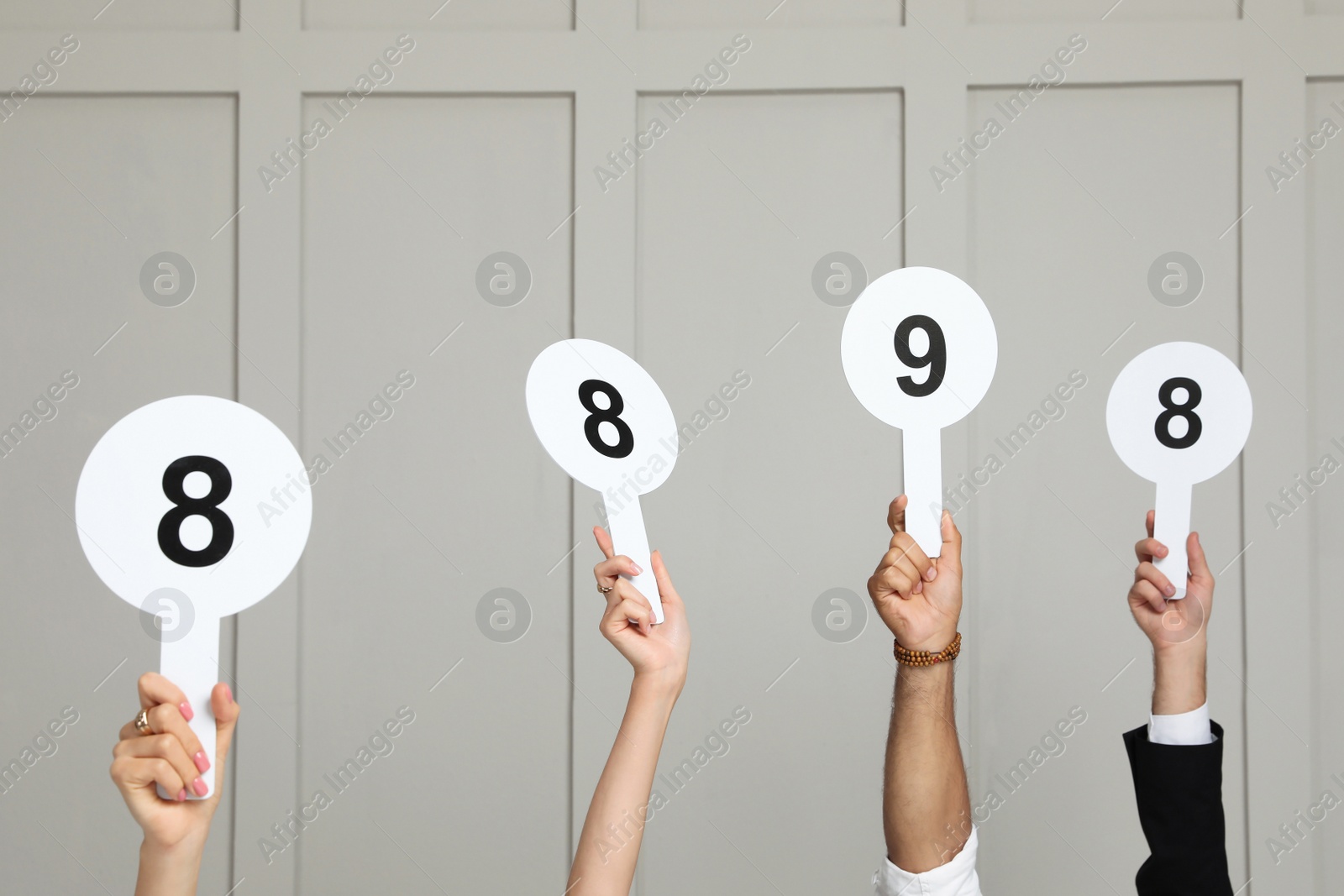 Photo of Panel of judges holding different score signs against light wall, closeup