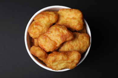 Photo of Bucket with delicious chicken nuggets on black background, top view
