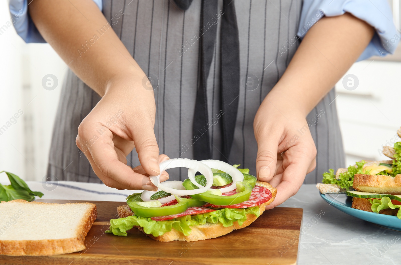 Photo of Woman adding onion to tasty sandwich at light grey marble table, closeup