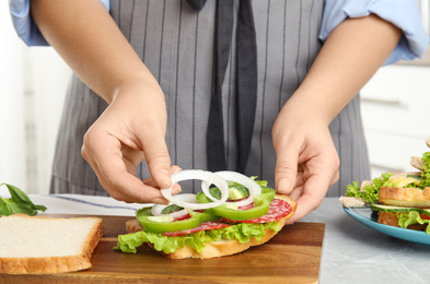 Photo of Woman adding onion to tasty sandwich at light grey marble table, closeup