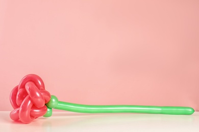Photo of Rose figure made of modelling balloon on table against color background. Space for text