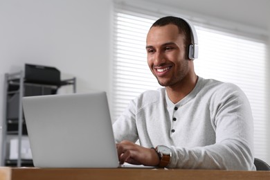 Photo of Young man with headphones working on laptop at table in office