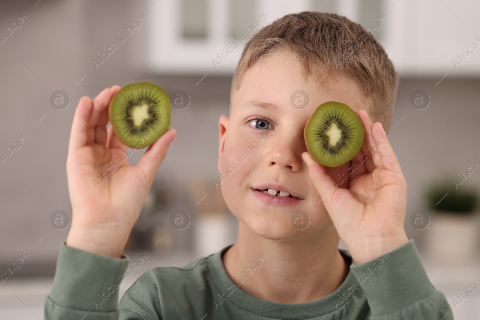 Photo of Cute boy with fresh kiwi at home