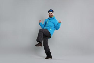 Photo of Winter sports. Cheerful man in ski suit and goggles on gray background