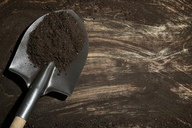 Photo of Metal shovel with fertile soil on dirty wooden surface, top view. Space for text