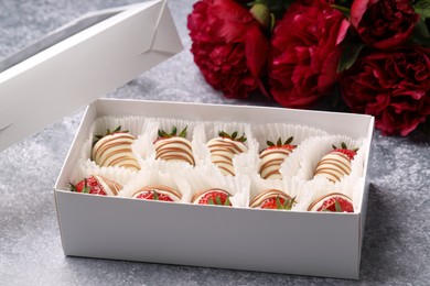 Delicious chocolate covered strawberries in box and flowers on light grey table