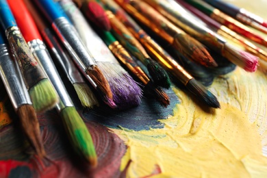 Photo of Different paint brushes on color palette, closeup
