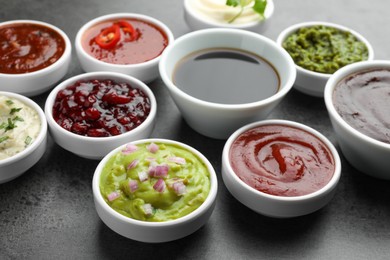 Photo of Different tasty sauces in bowls on grey table, closeup