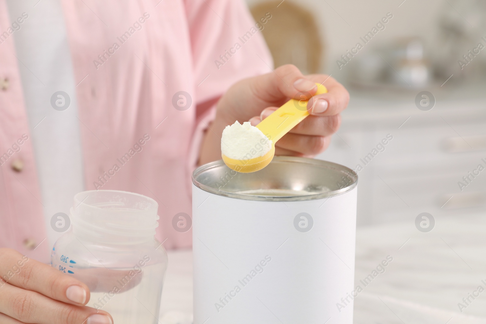 Photo of Woman preparing infant formula at table indoors, closeup. Baby milk