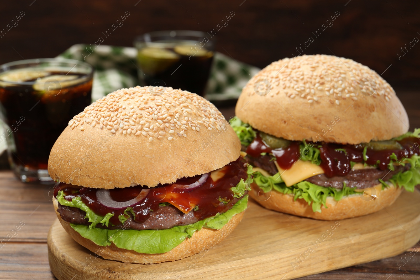 Photo of Board with delicious cheeseburgers on wooden table, closeup